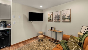 Een woonkamer met een flatscreen televisie, een koffiezetapparaat, een magnetron, een eettafeltje en een bank.