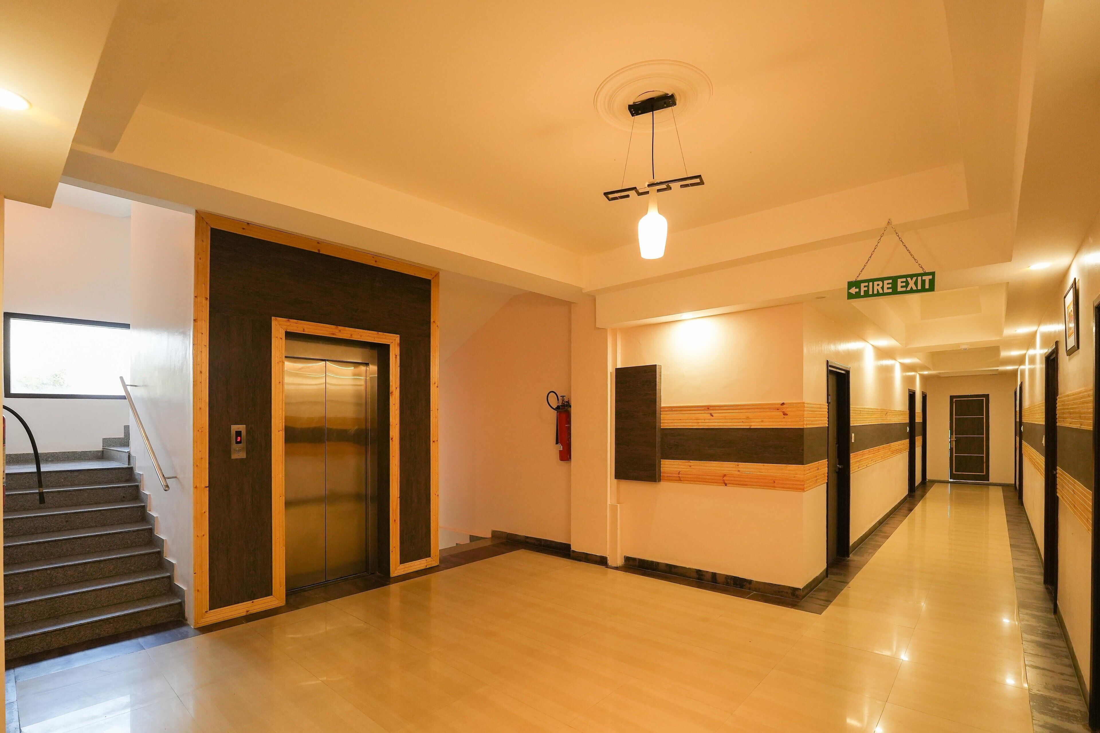 A hotel corridor with a fire exit sign, an elevator, and a staircase.