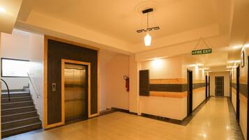 A hotel corridor with a fire exit sign, an elevator, and a staircase.