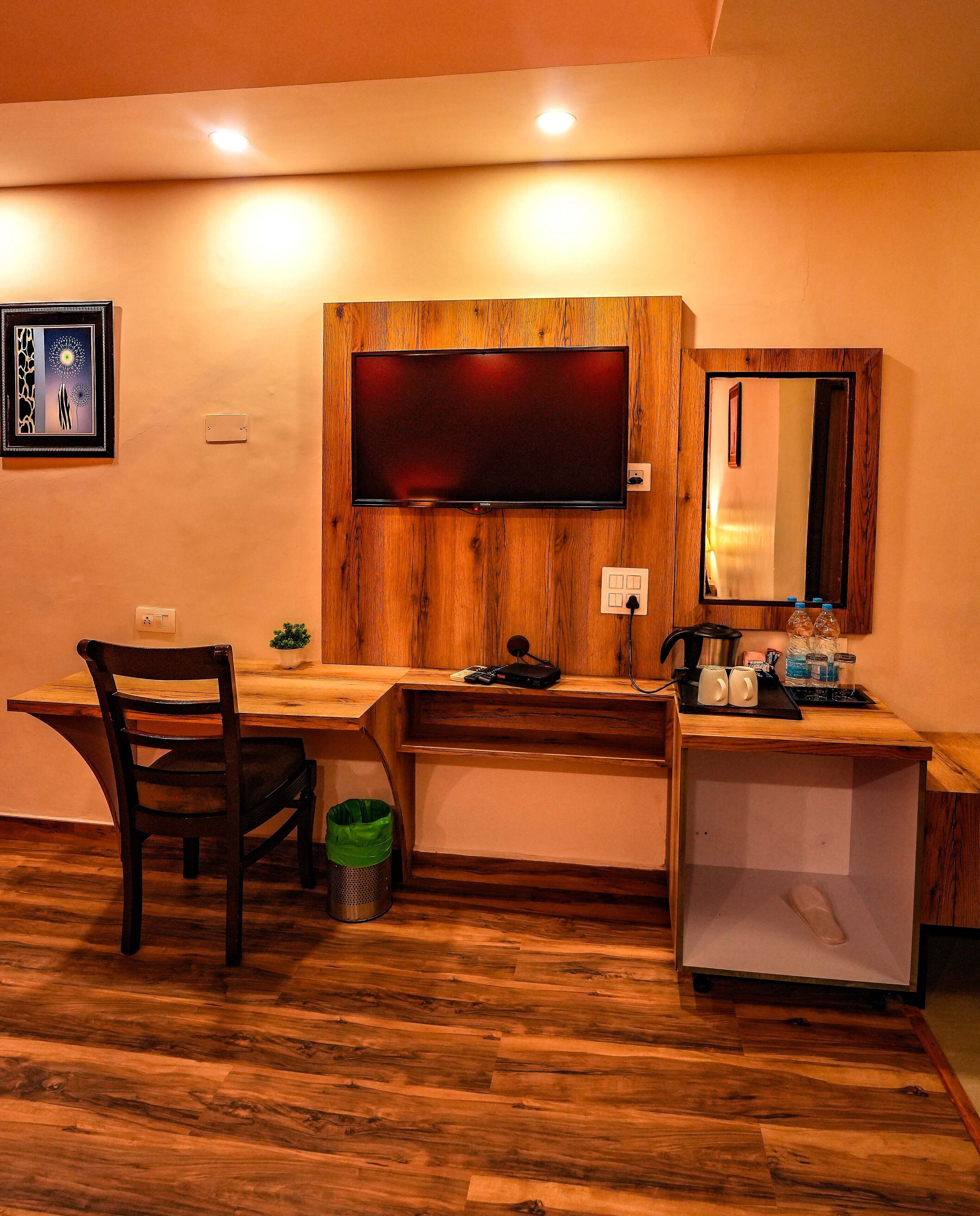 A wooden desk with a flat-screen TV, a chair, a trash bin, and a small mirror.