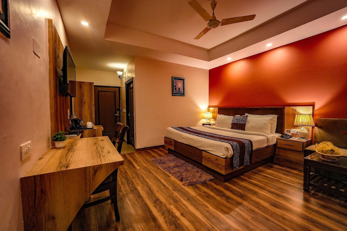 A bedroom with a wooden desk, a bed with a headboard, a nightstand, and a ceiling fan.