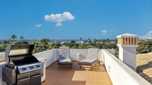 Una terraza en la azotea con una parrilla, dos sillones de descanso y vista al mar.