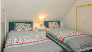 A bedroom with two beds, a nightstand with a lamp, and a door with a yellow frame. - Dookers' Hoose (Buckie)