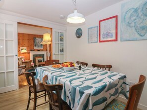 A dining area with a table set for four, wooden chairs, a bowl of fruit, and a white tablecloth with a whale pattern. - Dookers' Hoose (Buckie)