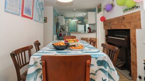 A dining area with a table set for two, chairs, a piano, and a fireplace. - Dookers' Hoose (Buckie)