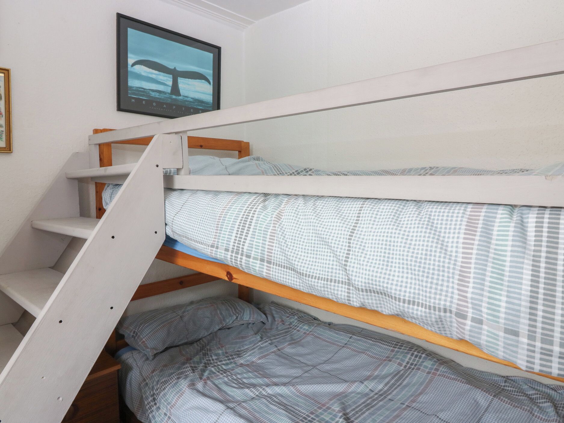 Una cama litera con estructura de madera y colcha a cuadros.