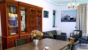 Uma sala de jantar com uma mesa de madeira, cadeiras, um vaso com flores e uma parede com uma imagem de um navio.