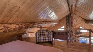 A cozy attic bedroom with a wooden sloped ceiling, a plaid armchair, a wooden dresser, and a bed. - Rustic Log Cabin - Close to Creede - Picturesque Views (Creede)