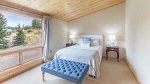 Ein Schlafzimmer mit großem Fenster, einem Bett mit Kopfteil, einem Nachttisch und einer blauen Polsterbank.