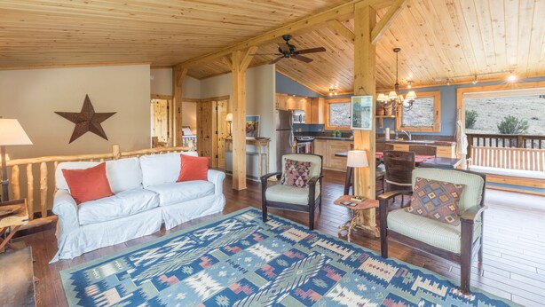 Ein gemütliches Interieur mit Holzbalkendecke, einer Sterndekoration, einem weißen Sofa, einem gemusterten Teppich und einer Küchenzeile mit Holzschränken und einem Fenster.