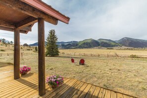 Une terrasse en bois avec une pergola, deux chaises rouges et une jardinière suspendue.