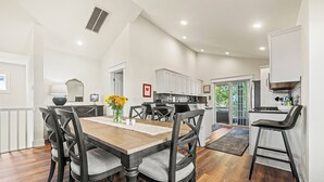 Un comedor con una mesa y sillas de madera, una cocina al fondo y vistas al exterior.