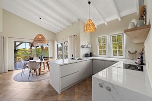 A modern kitchen with a large island, white cabinetry, and a dining area with a table and chairs. - Luxury Penthouse (Jan Thiel)