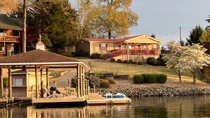 A lakeside cabin with a dock, a covered boat house, and a house with a red roof and porch. - Dockside Daze-Prime Waterfront Loc w/ Amazing View, Firepit, Tiki Bar, Lrg Dock (Moneta)