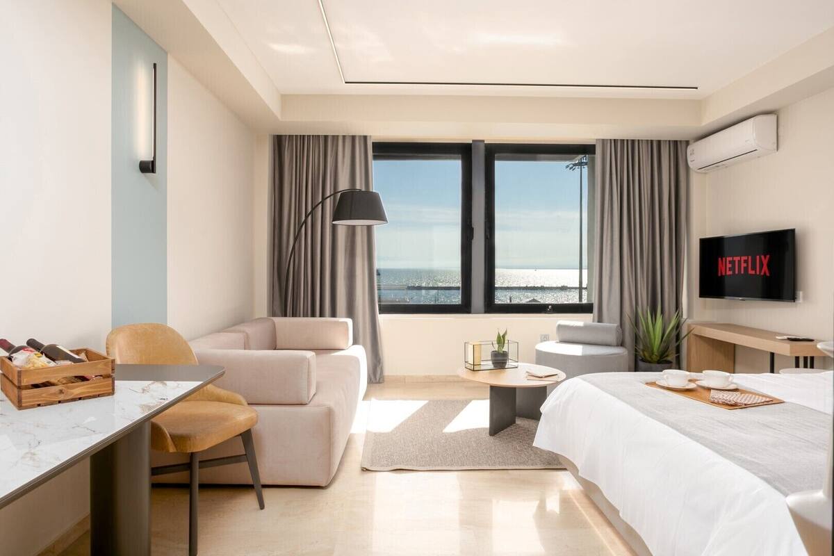 Een moderne hotelkamer met een groot bed, een bureau met een laptop, een stoel, een klein tafeltje met een plant en een televisie waarop 'NETFLIX' wordt getoond.