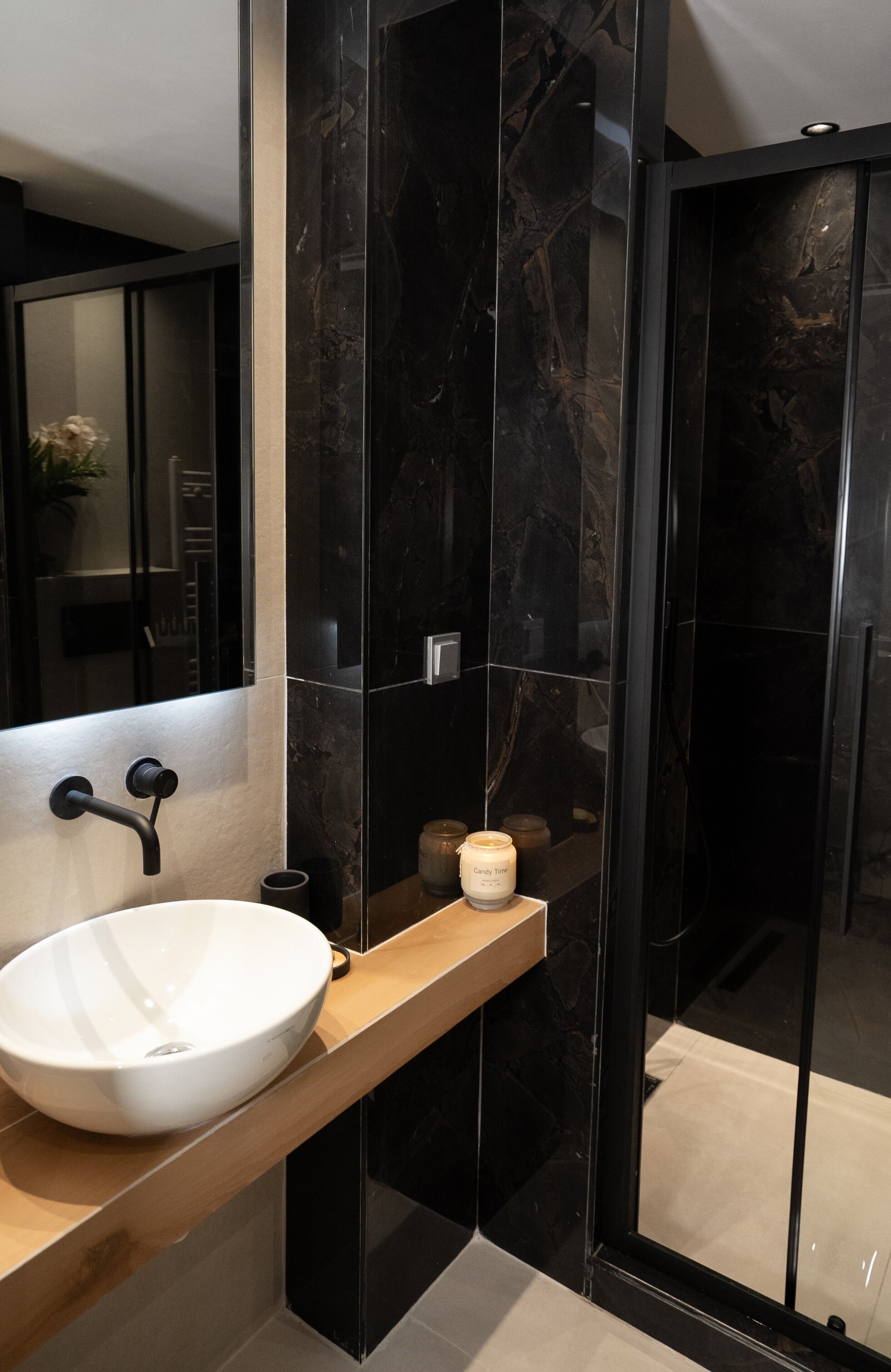 Une salle de bain moderne avec un grand lavabo blanc, un meuble-lavabo en bois et un mur en marbre noir.