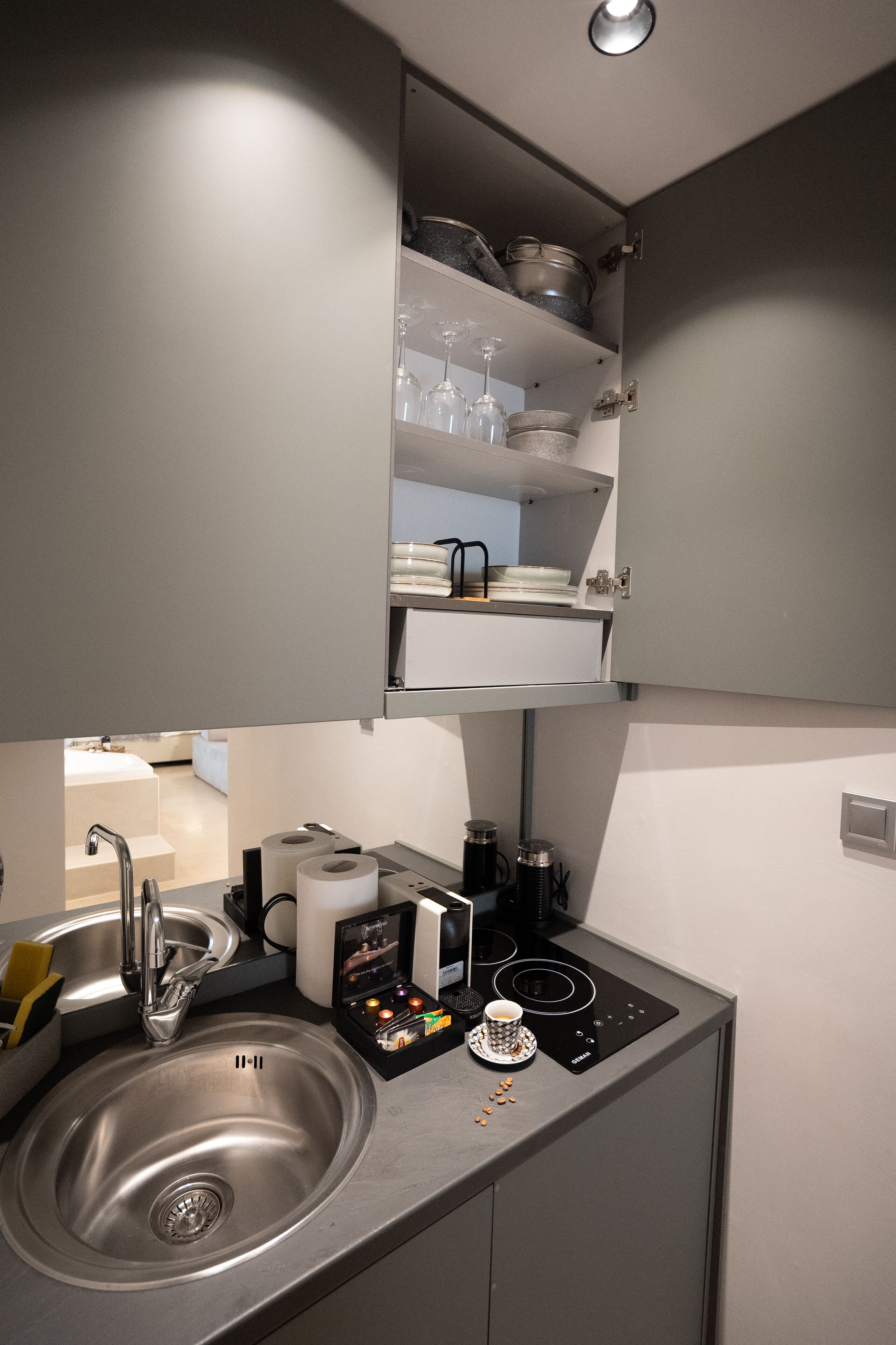 A compact kitchen with a sink, stove, and shelves above the counter.