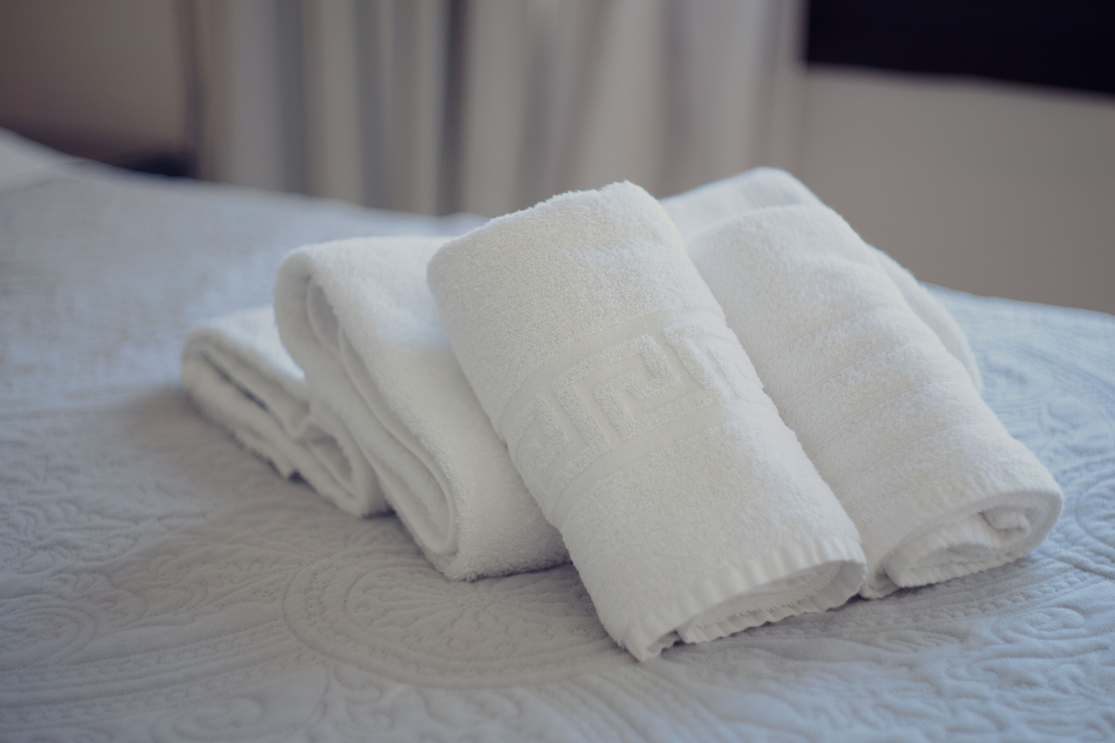 Neatly folded white towels stacked on a bed with a textured white bedspread.