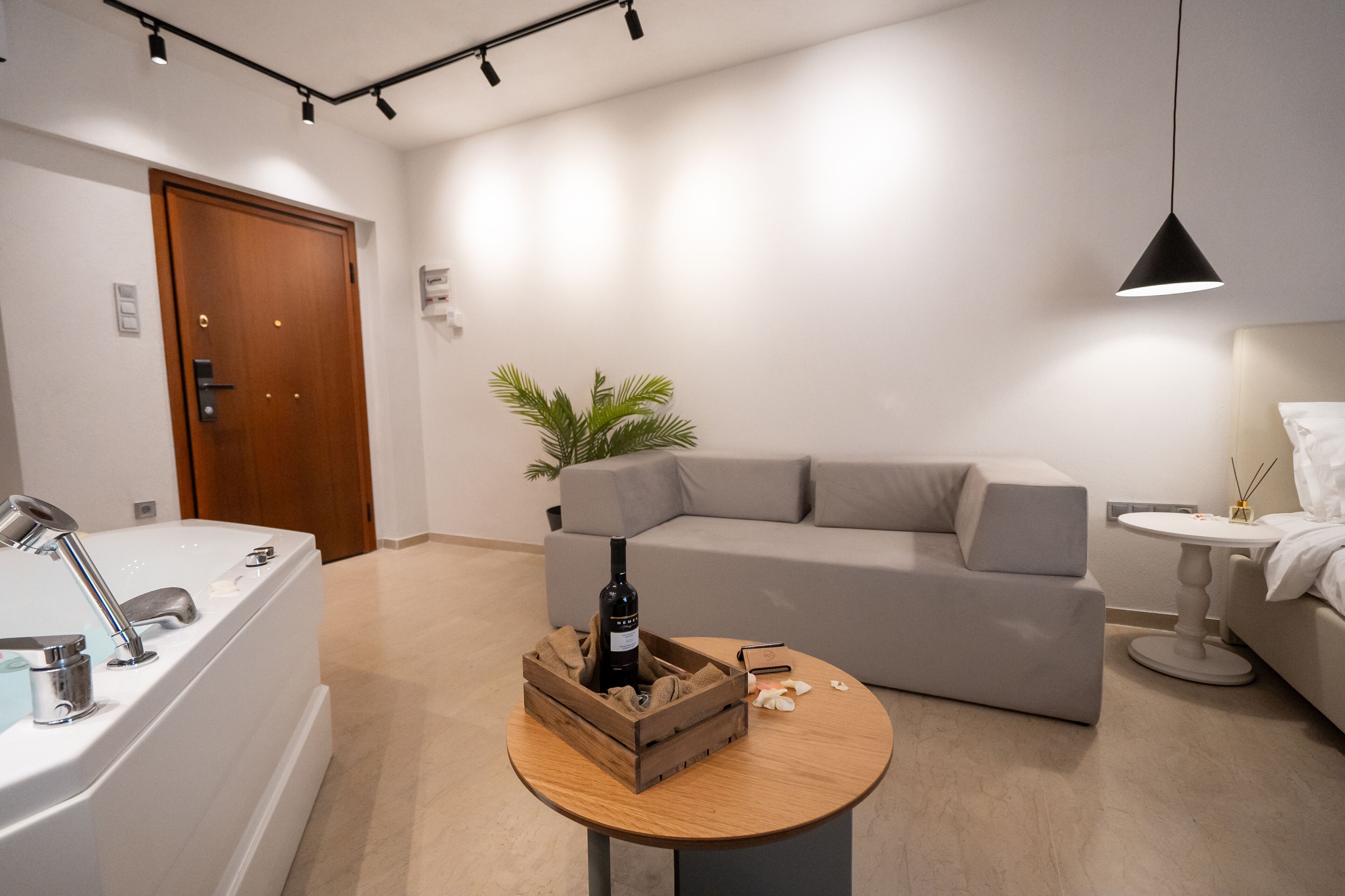 A modern living room with a bathtub, a wooden crate with a bottle, a grey sofa, and a small round table.