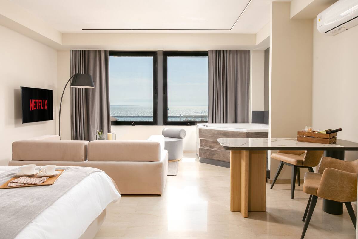 Een moderne hotelkamer met een bed, een bank, een eettafel en een televisie waarop het Netflix-logo te zien is.
