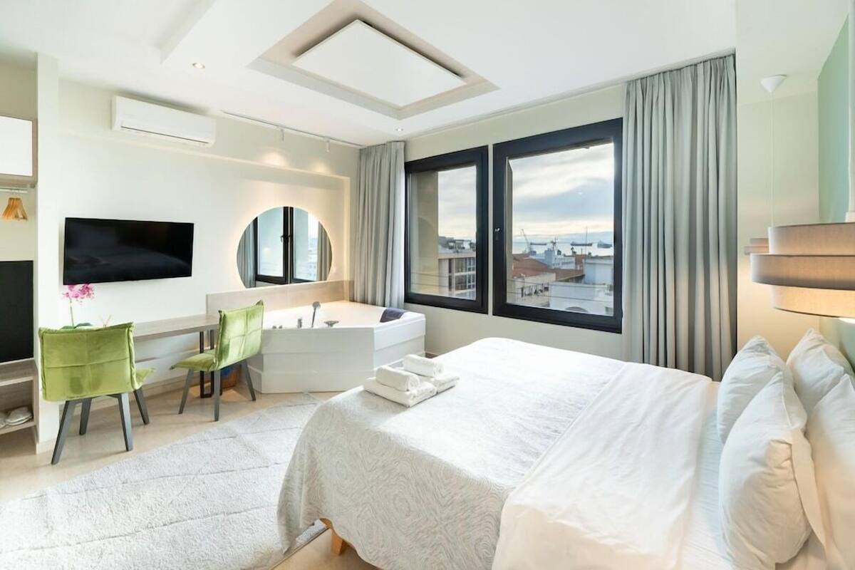Een hotelkamer met een groot bed, een bureau met stoel, een badkuip, een televisie en uitzicht op de stad.