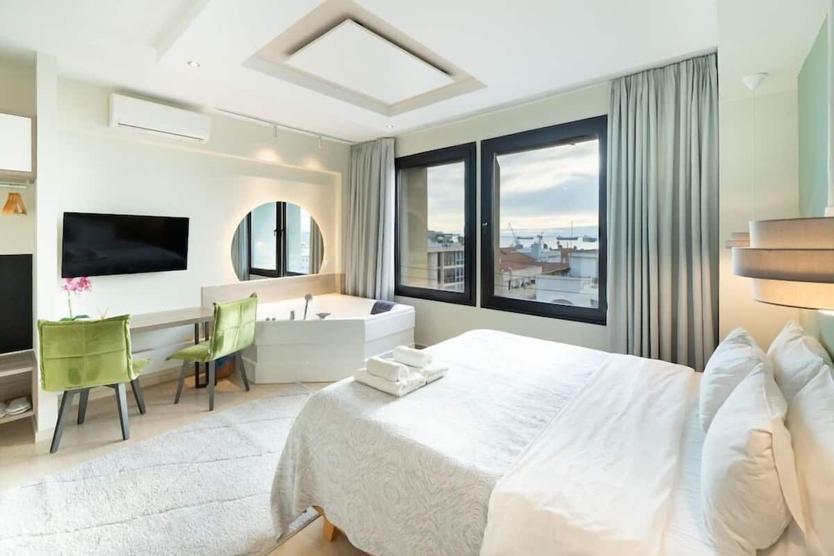 Habitación de hotel con una cama grande, un escritorio con silla, una bañera, un televisor y vistas a la ciudad.