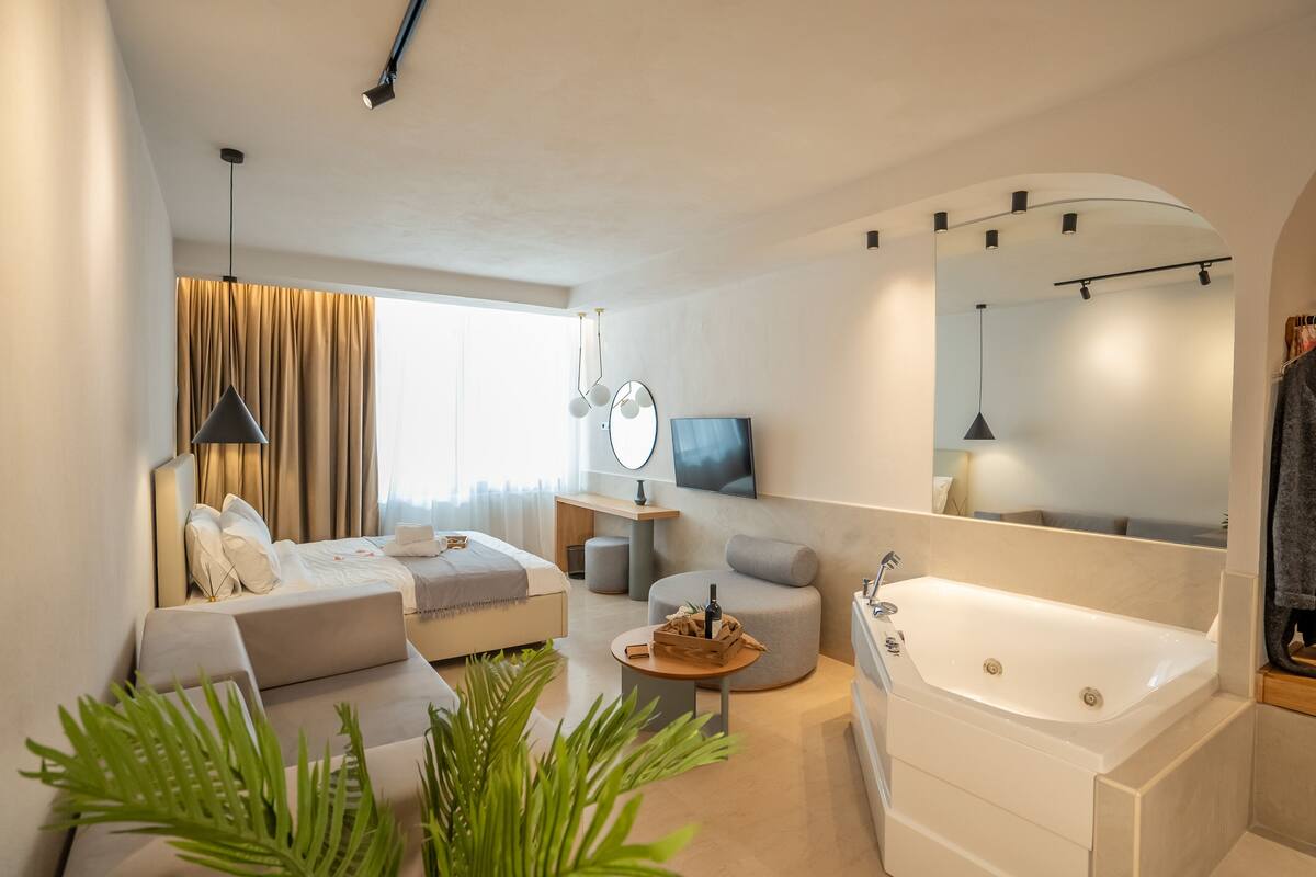 Een moderne hotelkamer met een bed, een bank, een rond bijzettafeltje en een groot bad.