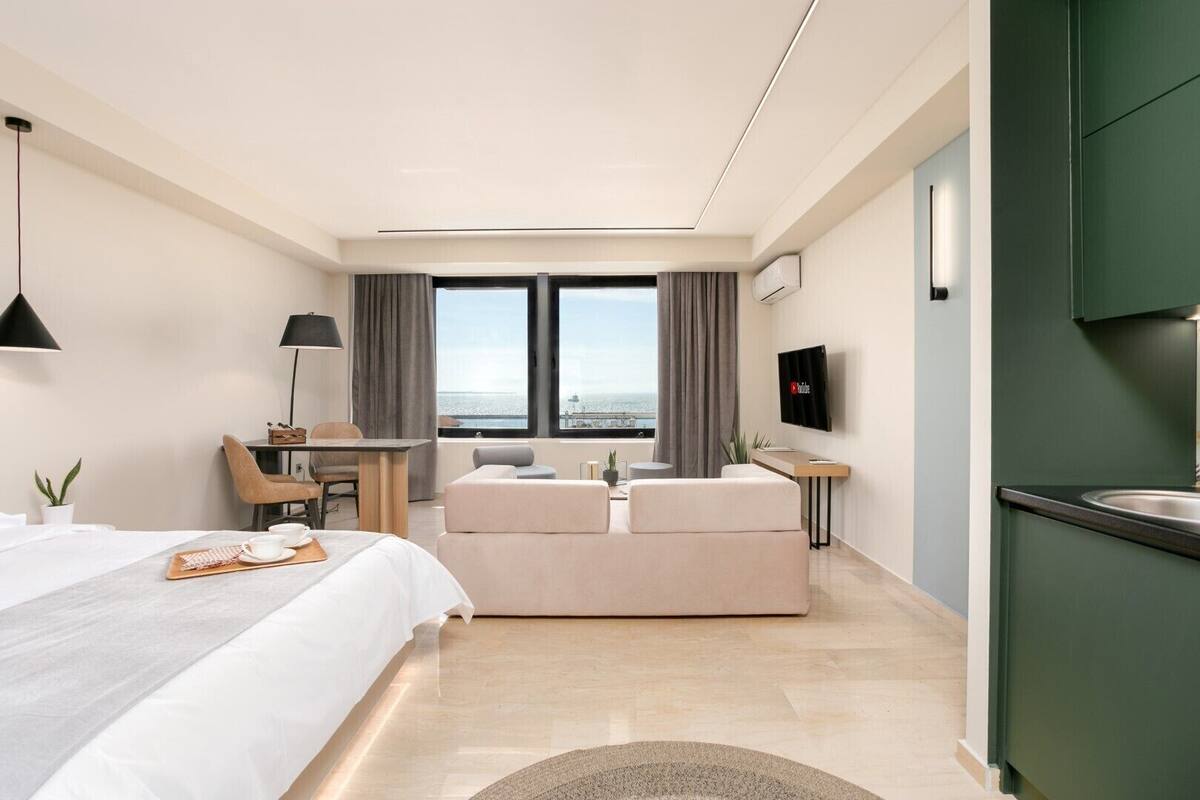 Een moderne hotelkamer met een bed, een zithoek met een tafel en stoelen, een televisie en uitzicht op zee.