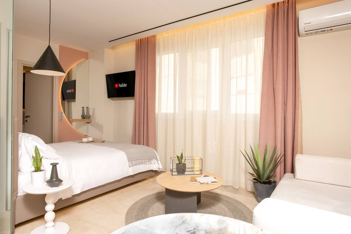 Een moderne hotelkamer met een bed, een sofa, een klein rond tafeltje, een aan de muur bevestigde televisie en een kamerplant.