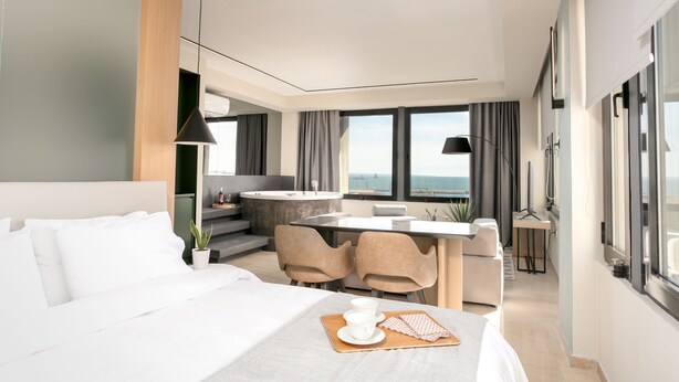 Een moderne hotelkamer met een bed, een zithoek en uitzicht op zee.