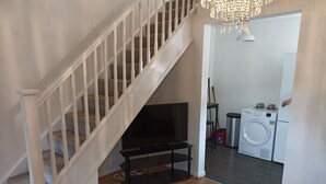 A staircase with a TV in the living room, a washing machine, and a chandelier.