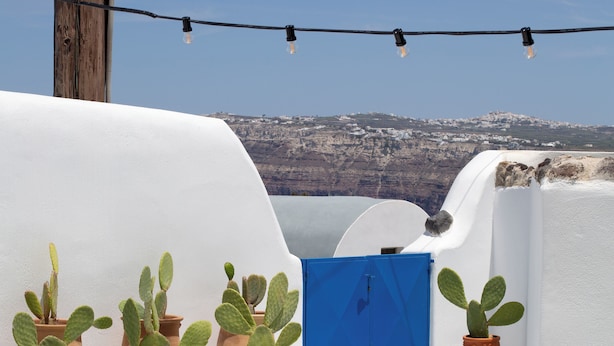 A rooftop terrace with white walls, terracotta pots with cacti, a blue gate, and a clear view of a mountainous landscape. - Amphora Villas Santorini Akrotiri (Santorini)