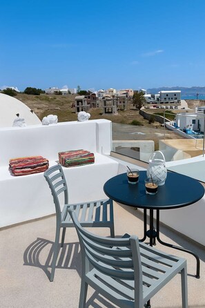 Une terrasse avec une table ronde, deux chaises et une vue sur les bâtiments qui bordent la côte.