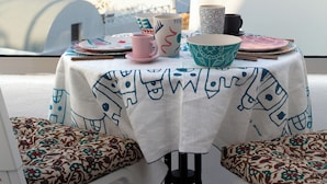 A table set with plates, cups, and a bowl on a balcony with a view of buildings and a mountain in the background. - Amphora Villas Santorini Akrotiri (Santorini)
