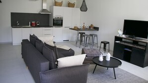A modern living room with a grey sofa, a small round table, and a TV on a black stand. - MAISON BAMBOU (Le Plan-de-la-Tour)