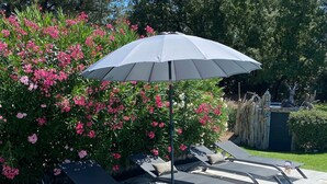 A poolside area with a wooden deck, lounge chairs, and a white umbrella. - MAISON BAMBOU (Le Plan-de-la-Tour)