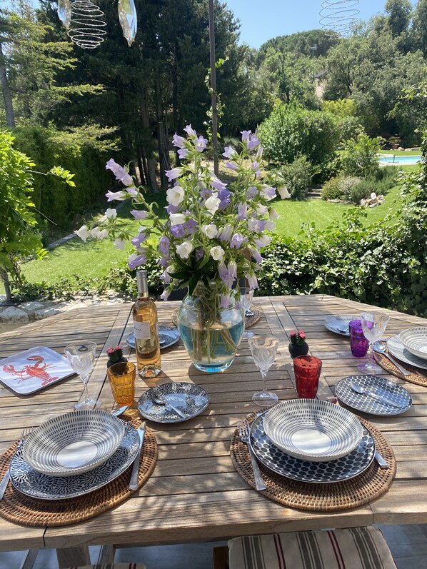 A wooden table set for a meal with plates, glasses, and a vase of flowers.