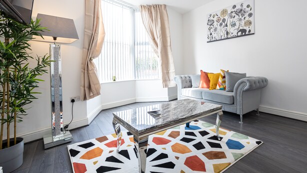 Una sala de estar moderna con un sofá gris, una mesa de centro, una lámpara y un ventanal con cortinas.