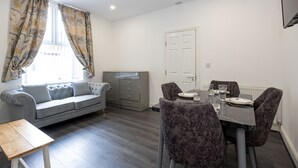Una sala de estar moderna con un sofá gris, una mesa de comedor con sillas y un aparador gris.