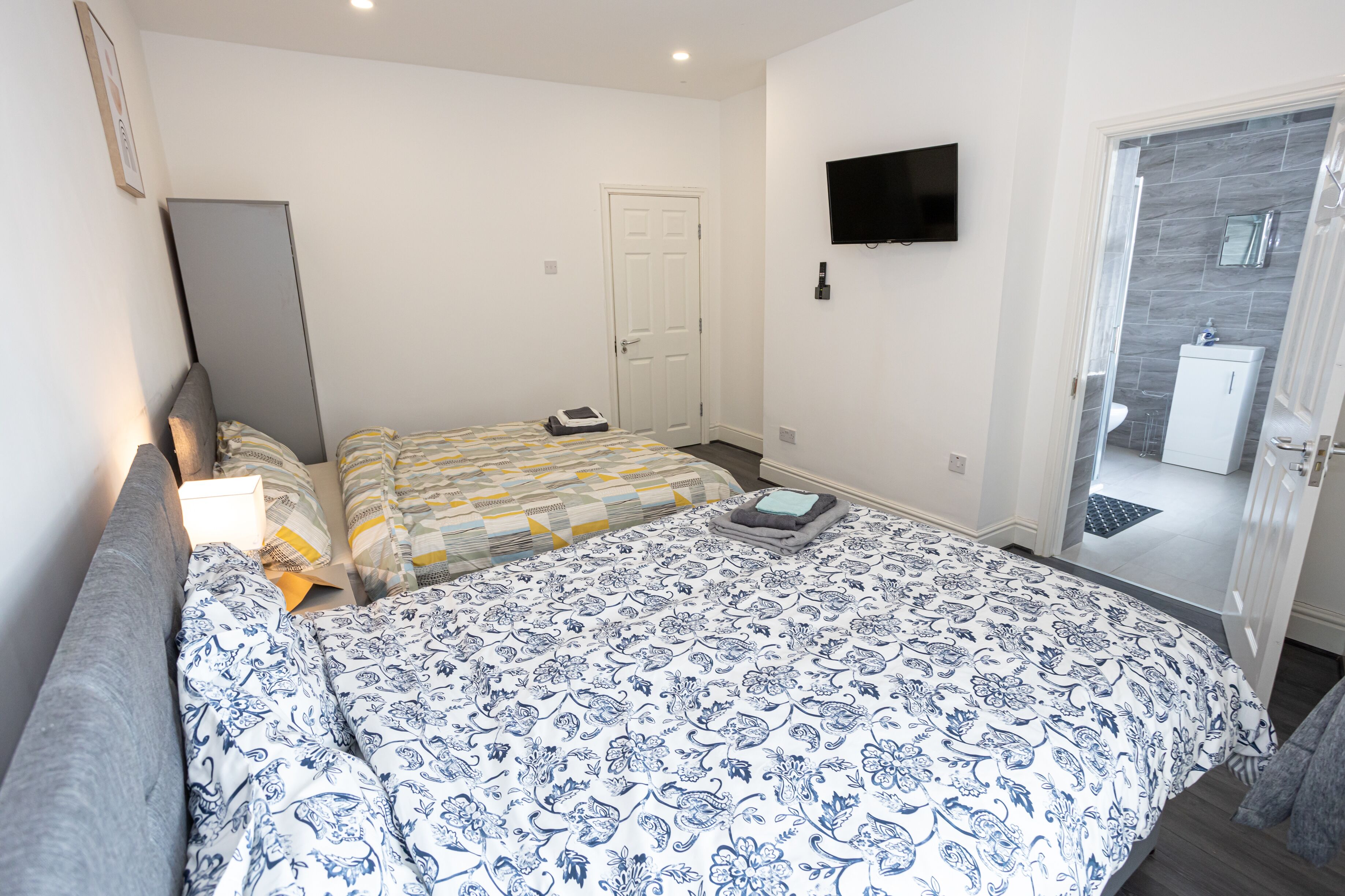 A bedroom with a large bed, a TV mounted on the wall, and a door leading to a bathroom.