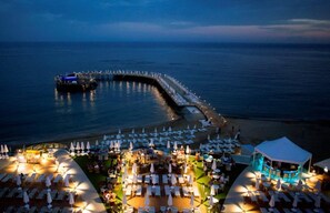 An outdoor dining area with tables and umbrellas, a pool, and a beachside walkway. - Azura Deluxe Resort & Spa Avsallar (Alanya)