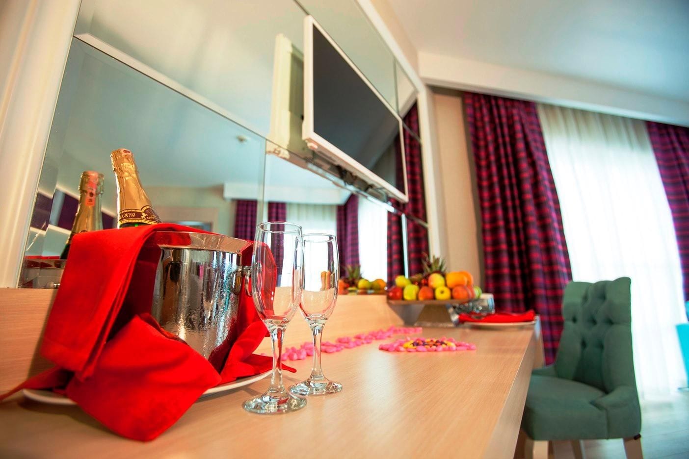 Ett hotellrum med en minibar, två glas, en flaska champagne, en fruktskål och en tv.