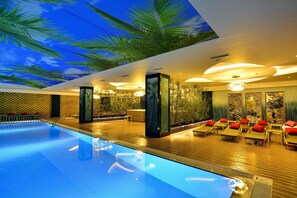 A modern indoor pool area with a ceiling mural, lounge chairs, and a reception desk. - Azura Deluxe Resort & Spa Avsallar (Alanya)