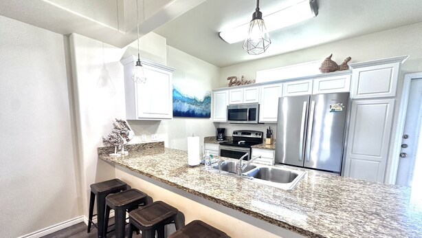 A modern kitchen with granite countertops, stainless steel appliances, and bar stools. - Condo w/3 Rooms, Heated Pool, and Close to Beach! (Corpus Christi)