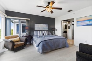 A modern bedroom with a large bed, a chair, a ceiling fan, and a view of the outdoors.