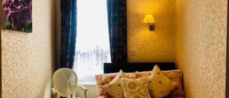 Una stanza piccola e accogliente con un letto, una sedia, una finestra con tende e una lampada a parete.