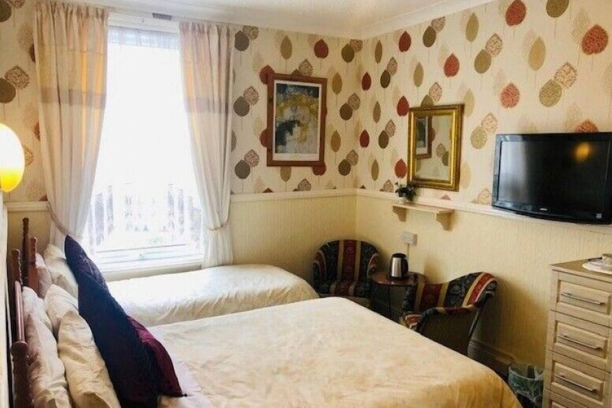 A hotel room with two beds, a television, a small table with a kettle, and a patterned wall.