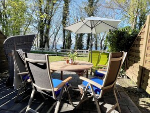 A patio with a round table, two chairs, an umbrella, and a view of trees and a fence.