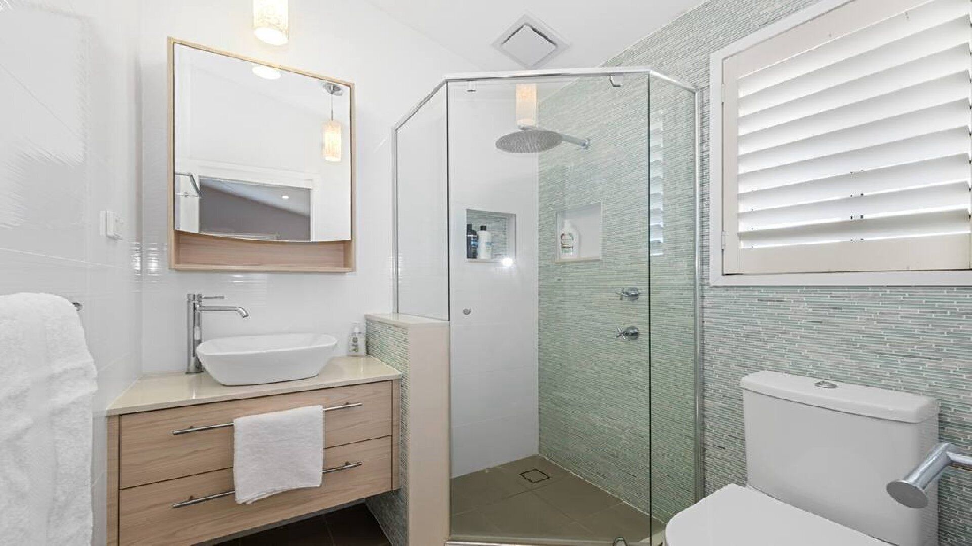 A modern bathroom with a glass-enclosed shower, a white sink, and a toilet.