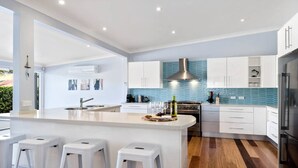 Et moderne køkken med hvide skabe, en central ø med barstole, en emhætte i rustfrit stål og en backsplash med blå fliser.